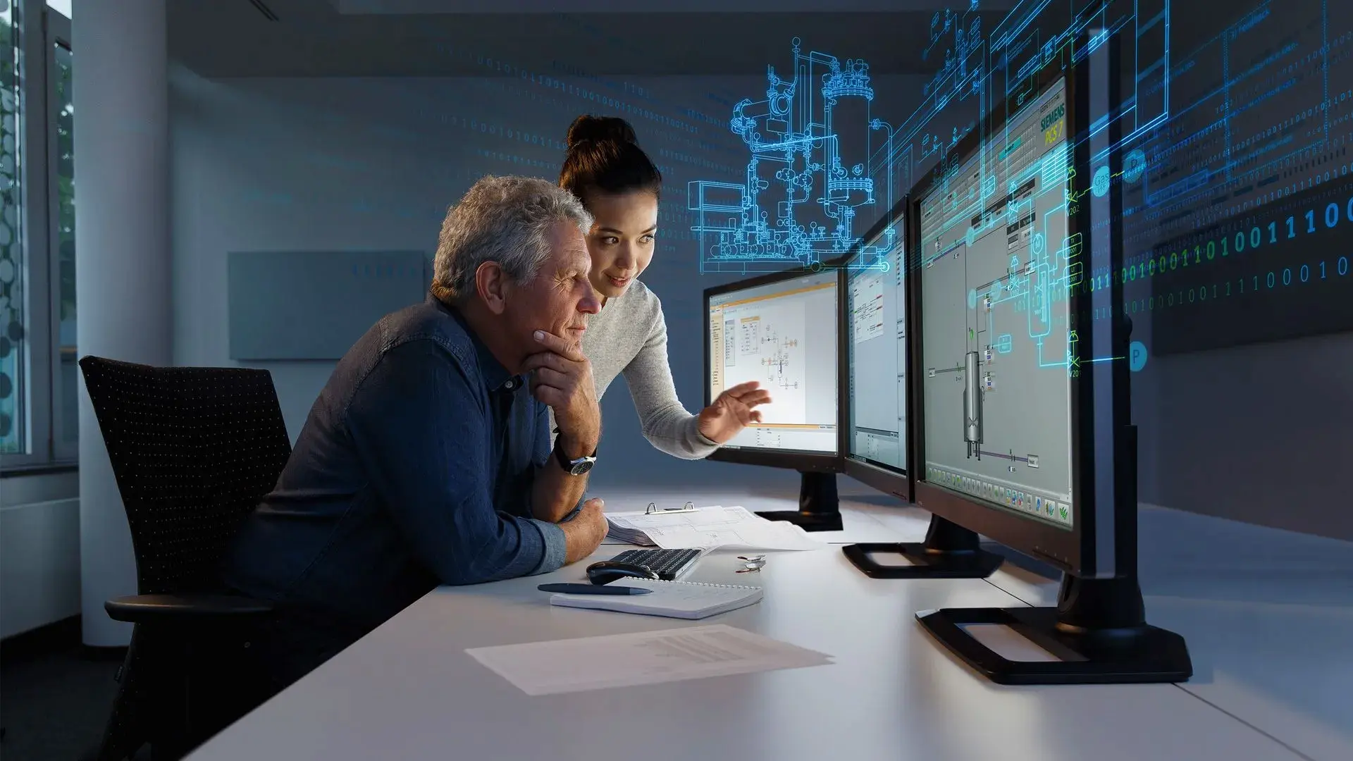A man and woman collaborate at computer screens, discussing digital designs and data