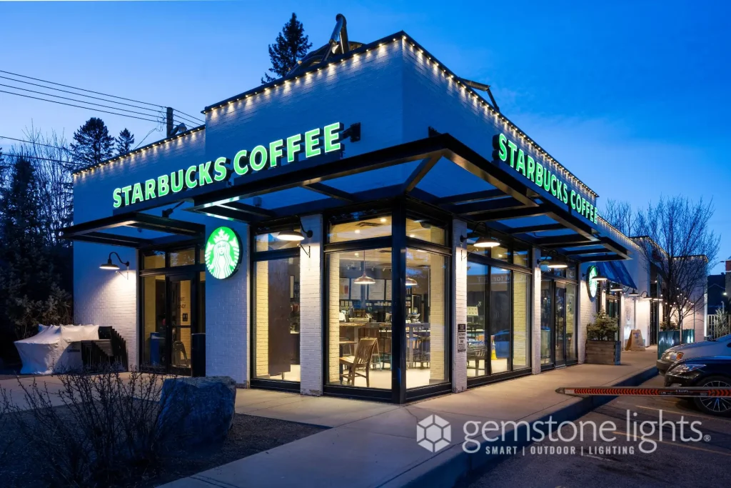 A brightly lit coffee shop displays its logo against a twilight sky