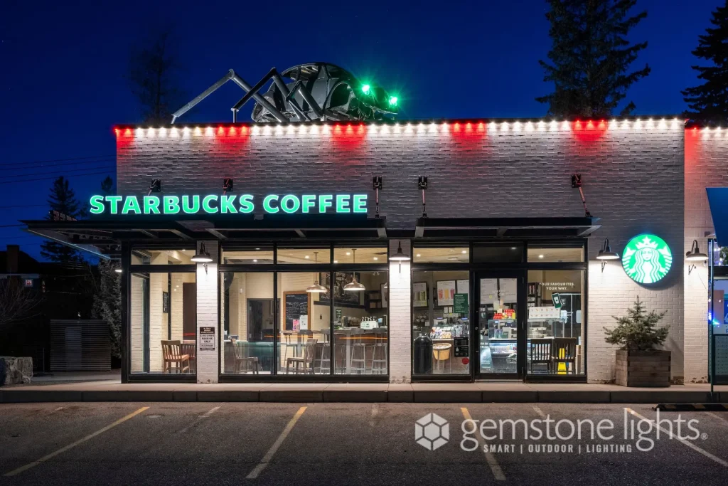 A brightly lit Starbucks storefront features outdoor seating under a twilight sky
