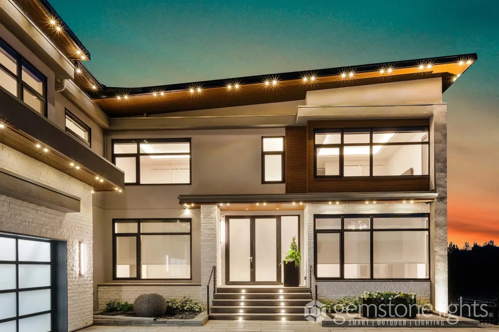 A modern house with large windows and illuminated exterior, set against a sunset sky