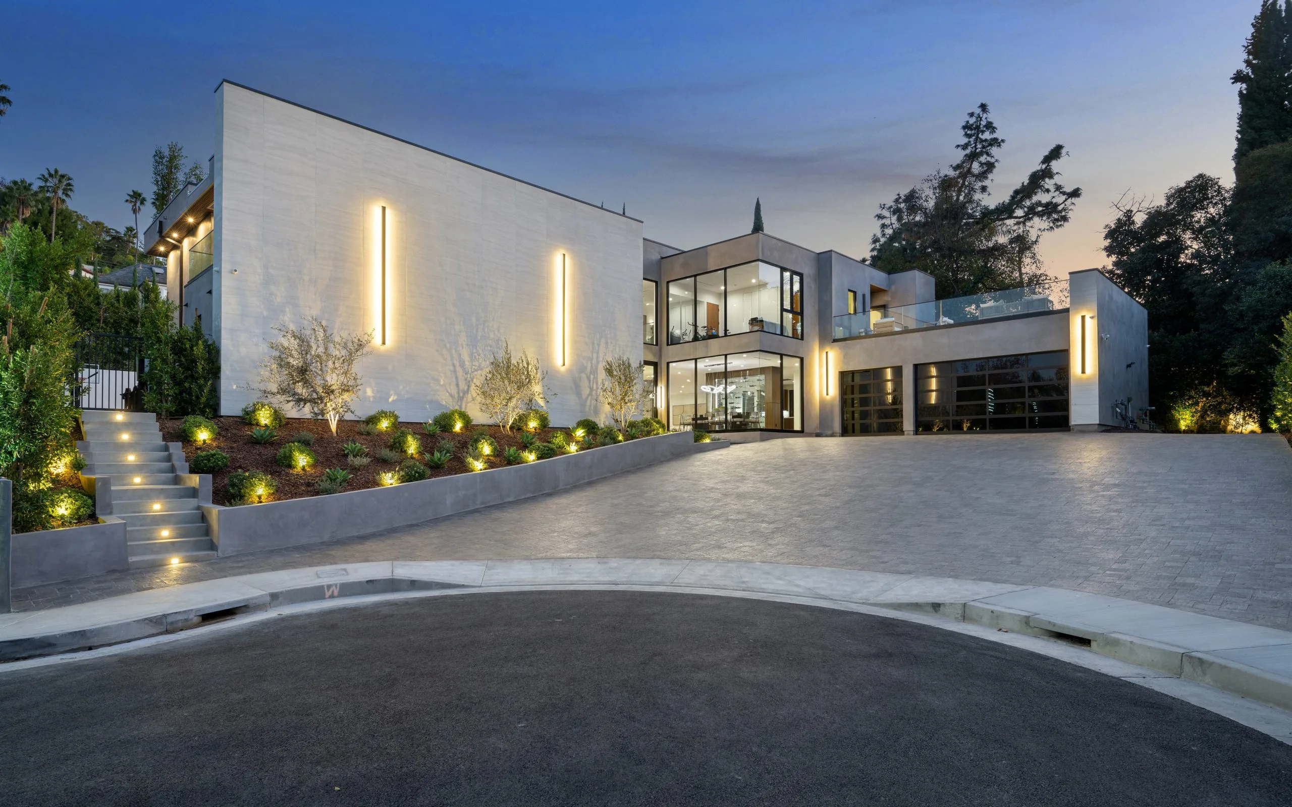 A modern home showcases sleek architecture and illuminated landscaping at twilight