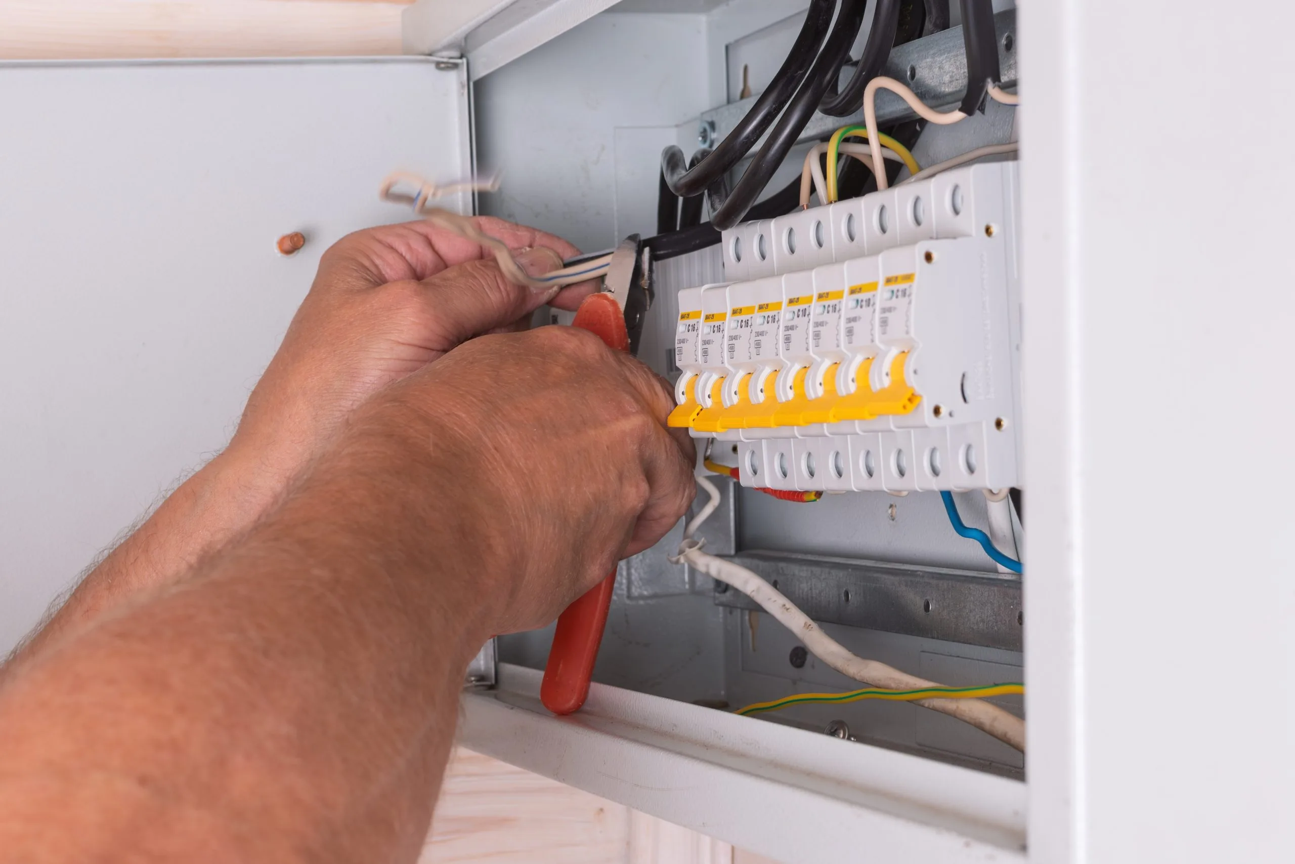 A person is using tools to connect wires in a circuit panel