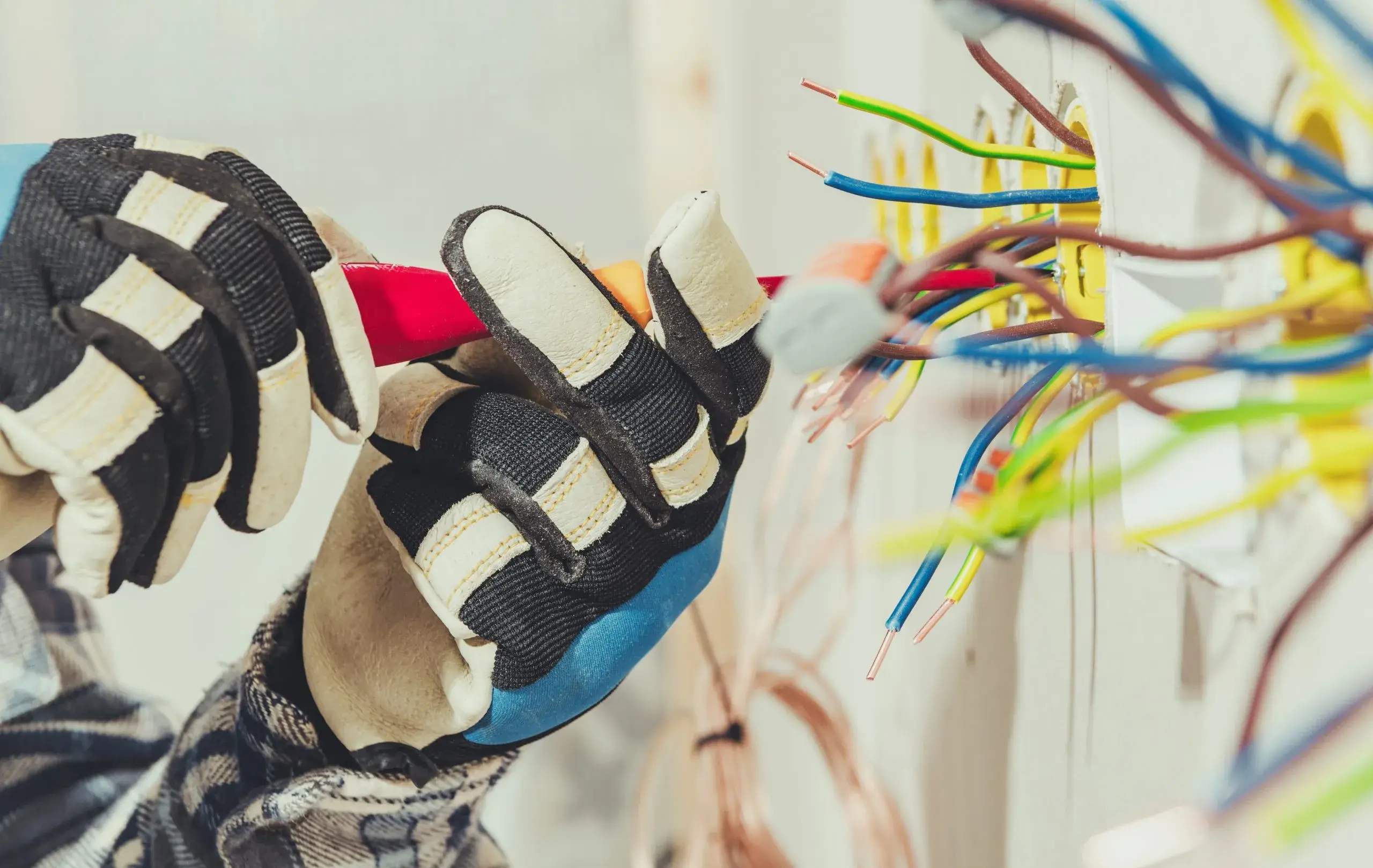A person in gloves is working on colorful electrical wires on a wall