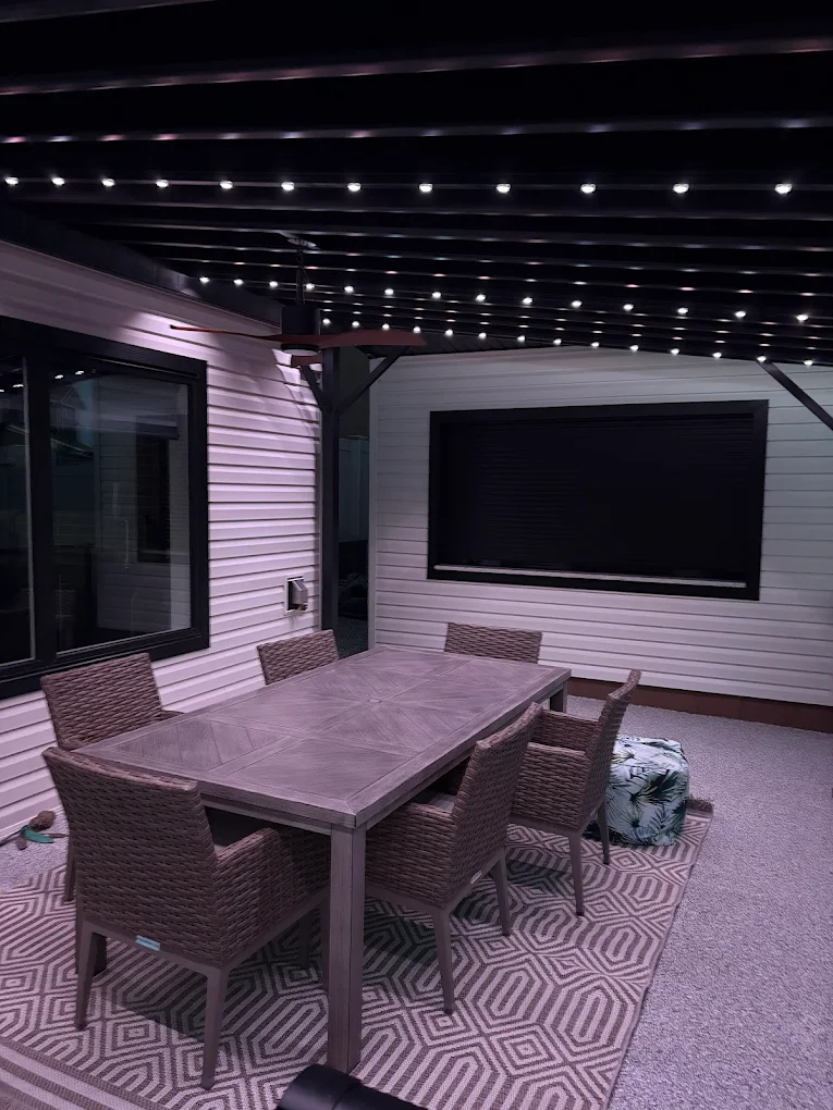 A stylish outdoor dining area features a table and chairs beneath twinkling lights