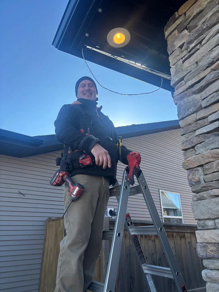 A person stands on a ladder, smiling while working on a light fixture
